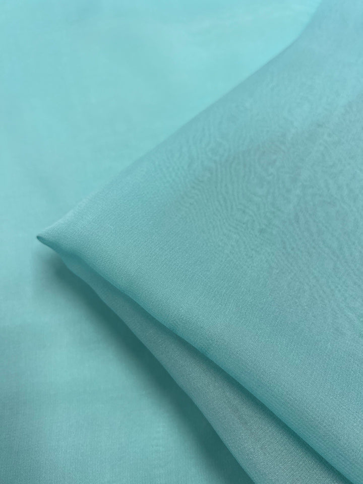 A close-up image of Silk Georgette - Tiffany - 135cm by Super Cheap Fabrics, neatly folded and laying on a flat surface. The lightweight fabric has a soft texture and a slightly translucent appearance, perfect for spring and summer outfits.