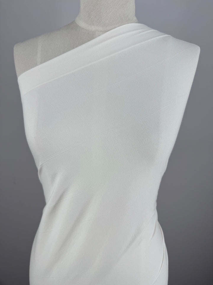 A white dress made of Super Cheap Fabrics' Cotton Lycra - Sugar Swizzle (135cm) is showcased on a mannequin against a gray background. The stretchy, medium-weight material gently hugs the body, enhancing its elegant silhouette.
