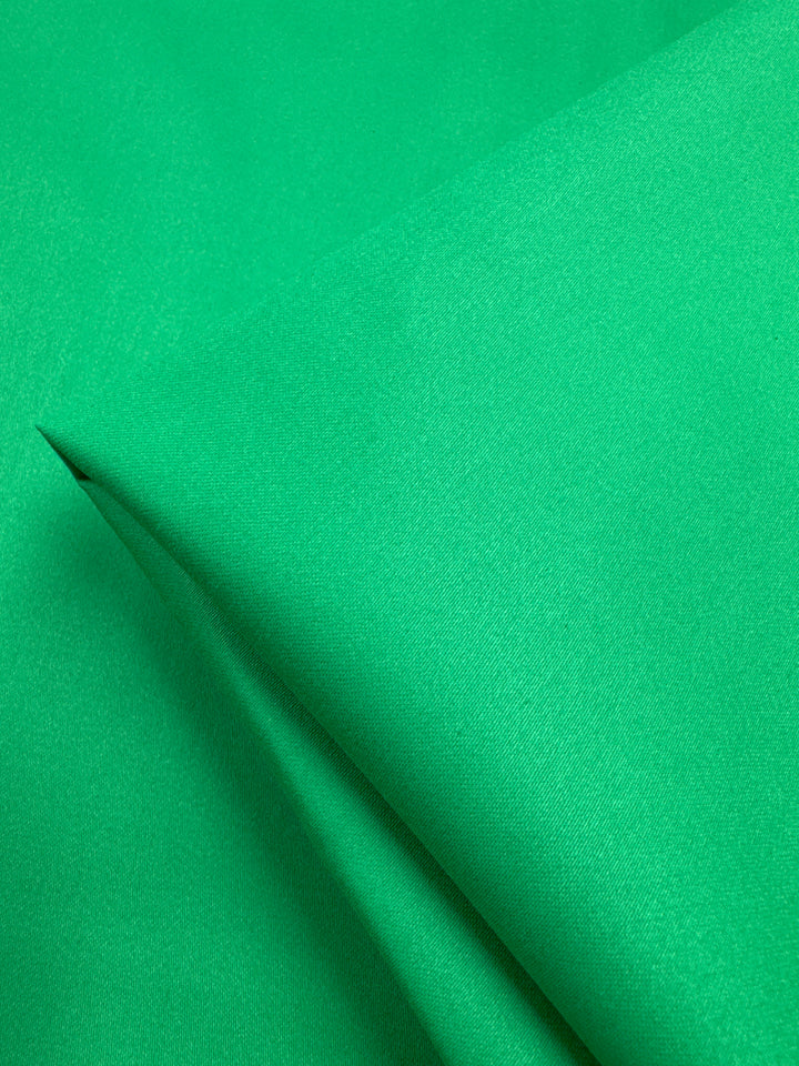 A close-up of Super Cheap Fabrics' Plain Sateen in Kelly Green (150cm) highlights its smooth, soft cotton texture and even color with a subtle fold.