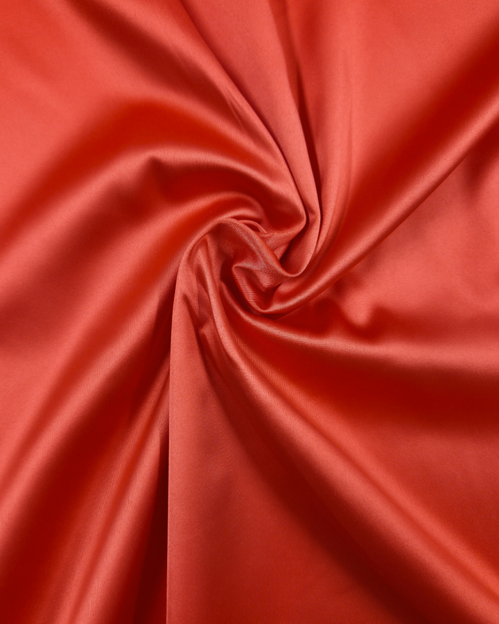 Close-up of Super Cheap Fabrics' Satin Deluxe in Grenadine, 150cm, twisted into a spiral pattern to showcase its smooth, glossy texture and shiny finish.