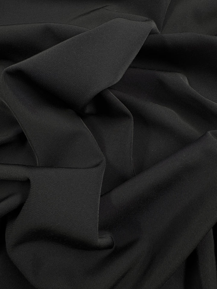 Close-up of Super Cheap Fabrics' Suiting - Black 4 Way- 142cm, showing its soft medium-weight texture and gentle folds that form wavy, overlapping patterns characteristic of 4-way stretch fabric.