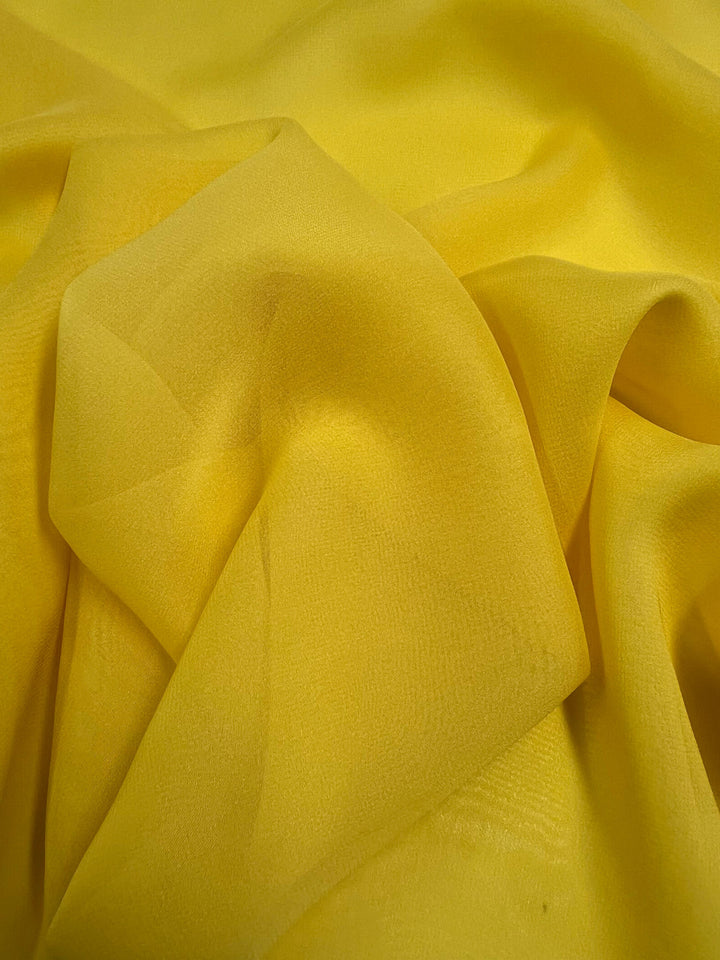 A close-up of crumpled Silk Georgette - Buttercup - 135cm from Super Cheap Fabrics reveals its soft textures and subtle folds. The lightweight fabric appears smooth, creating gentle shadows and highlights. Perfect for spring and summer outfits, it exudes an airy elegance.