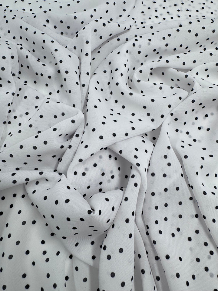 A close-up of Super Cheap Fabrics’ Printed Chiffon - Polka Dots (145cm) features white polyester chiffon with scattered black dots. The lightweight material, lightly gathered, forms soft folds and creases—ideal for sewing projects.