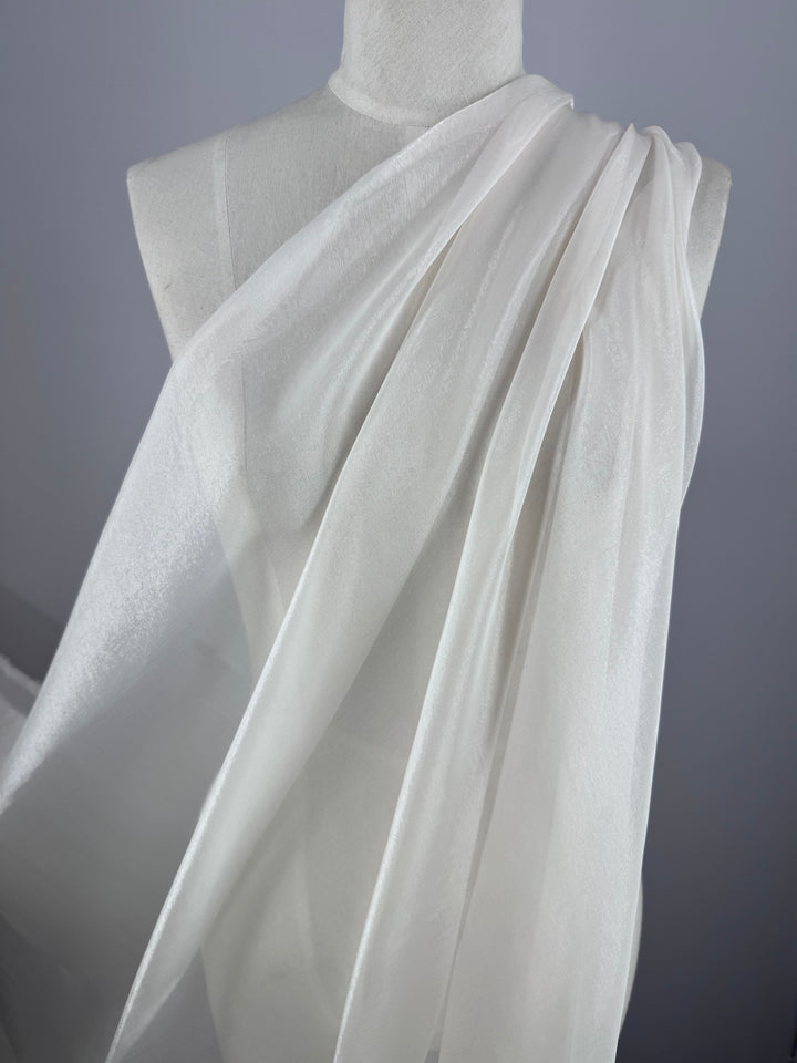 A white dress form is draped in Blended Silk Mousseline - Bridal Blush by Super Cheap Fabrics, styled like a classic toga. The sheer fabric elegantly cascades over the shoulder, evoking a bridal blush against the neutral gray background.