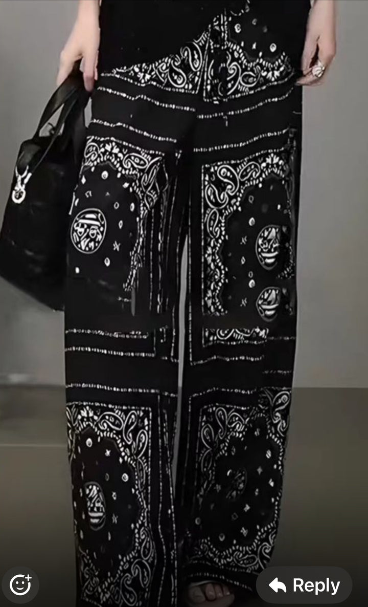 A person is wearing loose black pants made from Super Cheap Fabrics' Designer Rayon - Bandana Noir (148cm), featuring white paisley and celestial bandana prints, paired with a black handbag. Only the lower half of the body is shown.