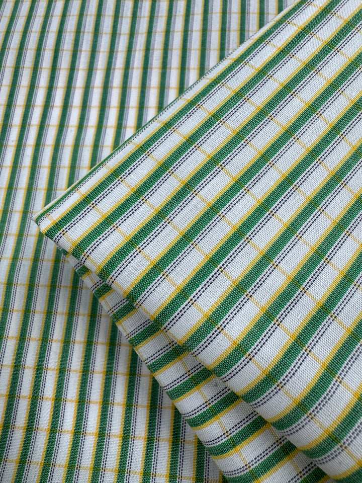 Close-up of Shirting - Harp - 112cm by Super Cheap Fabrics, a lightweight polyester cotton fabric with a green, yellow, and white checkered pattern, folded on a matching multi-colour background.