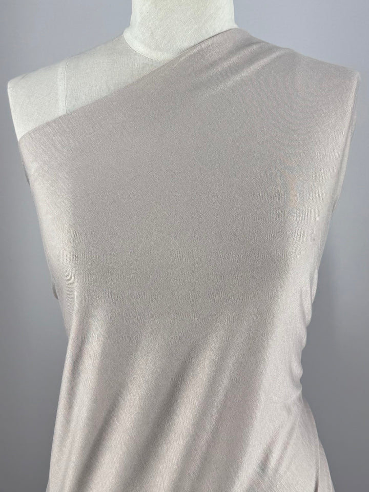 A mannequin displays a sleeveless, asymmetrical top in Super Cheap Fabrics’ Cotton Jersey - Oatmeal (150cm), featuring lightweight fabric and one exposed shoulder, set against a plain gray background.