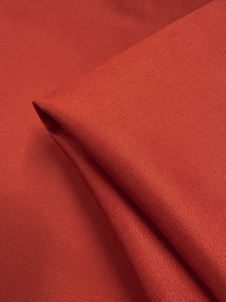 A close-up of Plain Sateen - Chili - 150cm by Super Cheap Fabrics, featuring its smooth texture and vibrant chili hue, neatly folded against a matching red background.