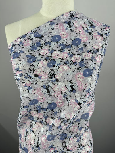 Set against a plain gray backdrop, the mannequin is draped in Super Cheap Fabrics' Designer Jacquard - romi - 145cm, a floral one-shoulder polyester with pink, blue, and white flowers on a dark background. The lightweight fabric boasts a textured appearance.