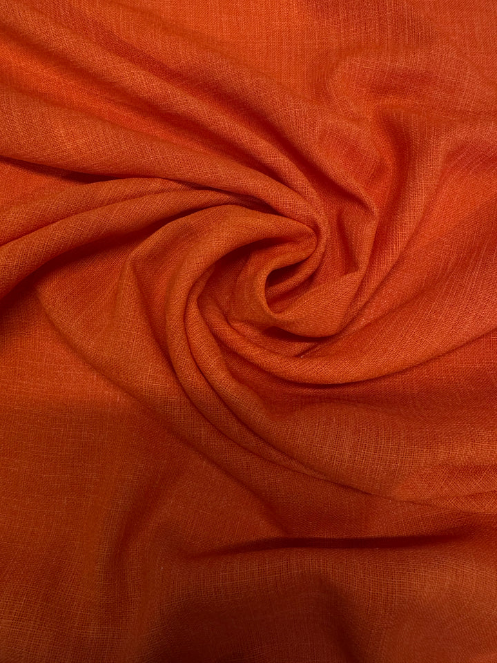 A close-up of Super Cheap Fabrics’ Crepe - Puffin’s Bill - 112cm, lightweight polyester in vibrant orange, gathered in a loose swirl with visible fine threads and natural folds—ideal for elegant evening gowns.