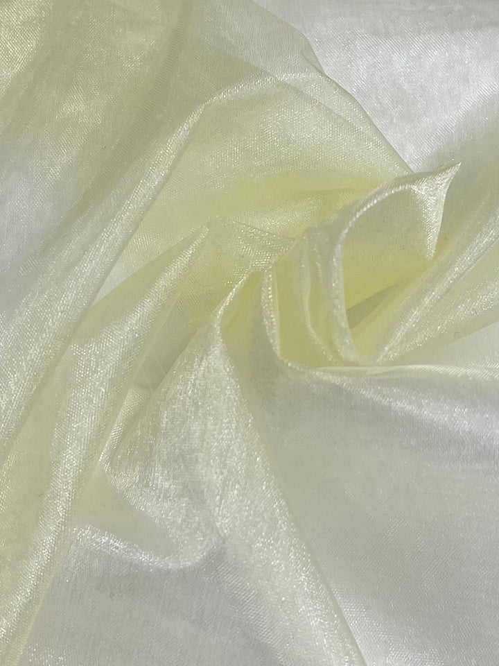 A close-up image of a piece of Organza - Pear Sorbet - 150cm fabric by Super Cheap Fabrics. The light yellow organza material is crumpled and folded, creating gentle waves and soft shadows. This lightweight fabric appears delicate and slightly glossy, reflecting light to give a subtle shimmer.