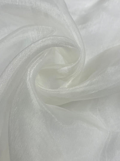 A close-up image of the "Organza - Ivory - 150cm" fabric by Super Cheap Fabrics, slightly gathered and swirled to create soft folds and a delicate texture. The material appears lightweight and semi-translucent, showcasing a subtle shimmer under the light.