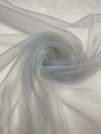 A close-up of Super Cheap Fabrics' Organza - Illusion Blue - 150cm shows sheer fabric swirling gently on white, creating delicate folds and a translucent, ethereal look.