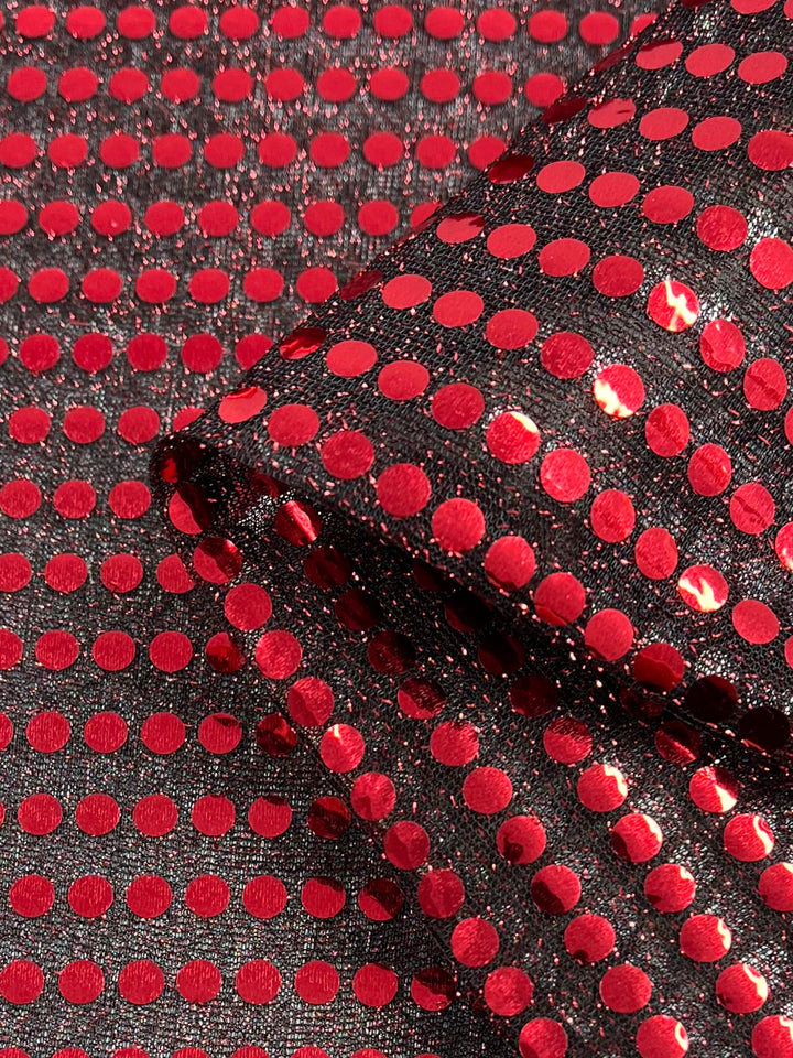 A close-up of Super Cheap Fabrics' Sequin - Black & Red - 112cm shows shiny red sequins in a polka dot pattern on sheer black material, with part of the fabric folded over itself.