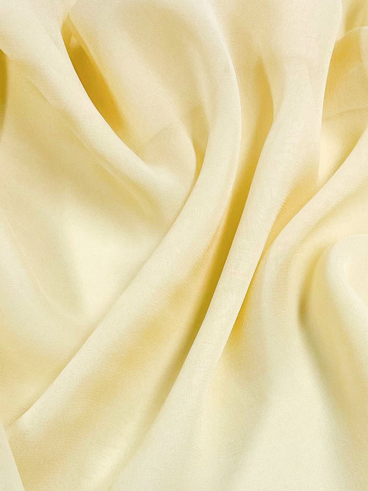 Close-up of soft, flowing Silk Georgette - Butter from Super Cheap Fabrics, showcasing its gentle folds and translucent, light-yellow texture. This 135 cm wide lightweight fabric features a smooth, airy appearance, perfect for crafting spring and summer outfits that evoke delicacy and elegance.