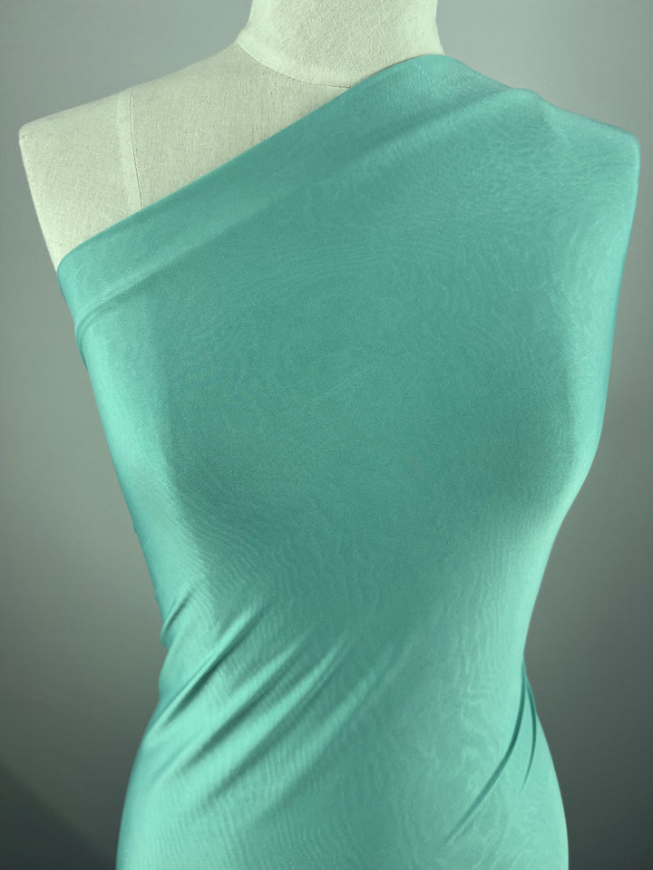 The dress form is draped in Super Cheap Fabrics’ Plain Lycra - Mist - 140cm, a stretchy fabric covering one shoulder and hugging the torso to showcase its smooth texture and drape, perfect for form-fitting garments.