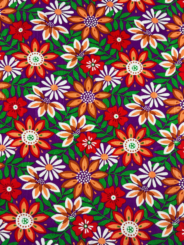 A lively and cheerful fabric pattern named "Lolita Autumn," featuring vibrant flowers in red, orange, white, and purple with green leaves and stems. Crafted from lightweight rayon by Super Cheap Fabrics, the flowers are arranged in a repeating pattern on a deep blue or purple background. The fabric measures 145cm wide.