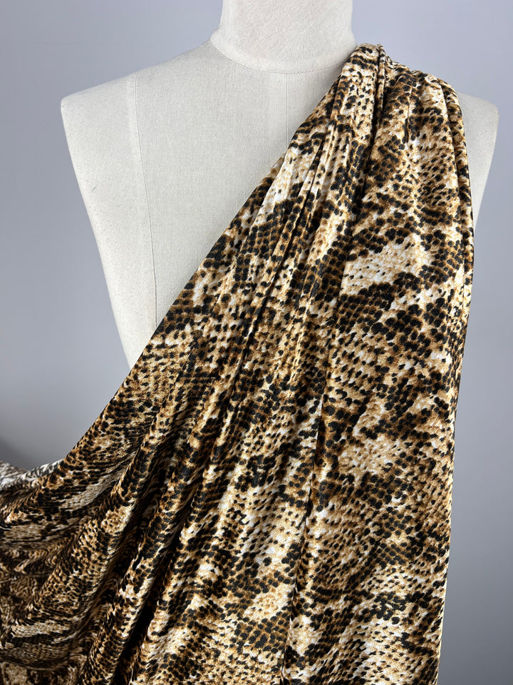 Super Cheap Fabrics’ Printed Velvet - Python is a 150cm wide, light to medium weight polyester with a brown, black, and cream snakeskin print draped over a white dress form against a neutral background.