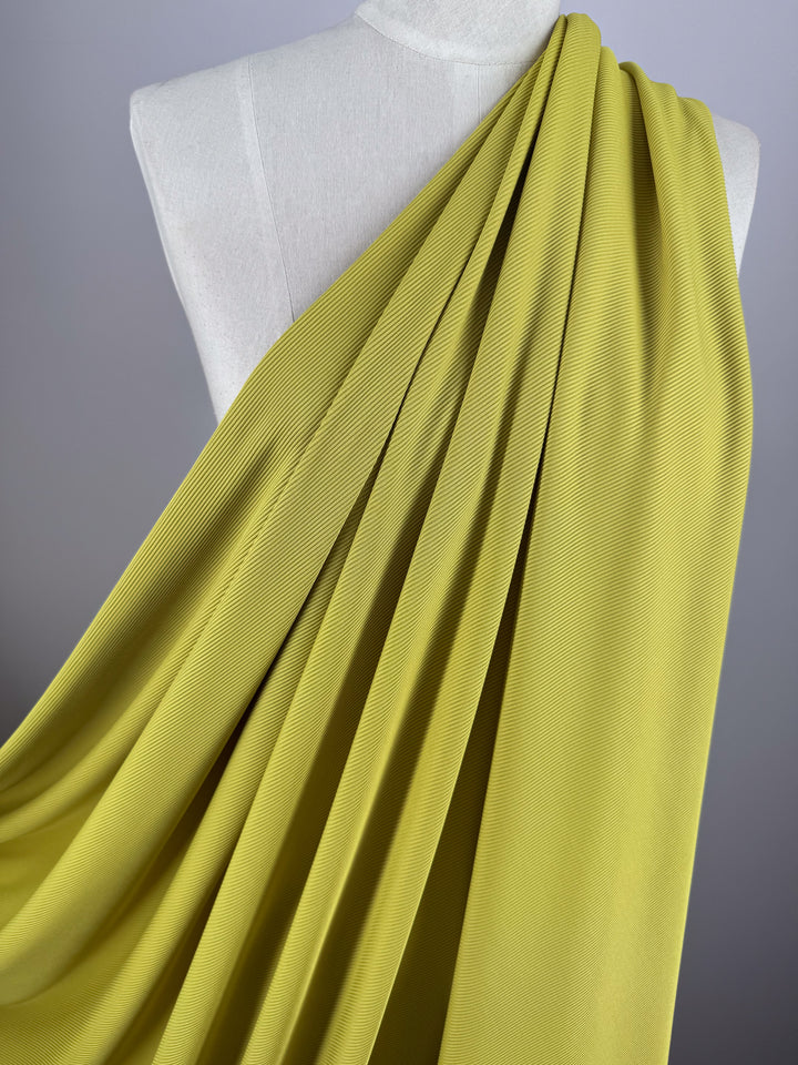 The Rib Knit 1x1 - Squash by Super Cheap Fabrics flows elegantly over a white mannequin torso, highlighting its smooth texture and folds against a plain gray background.