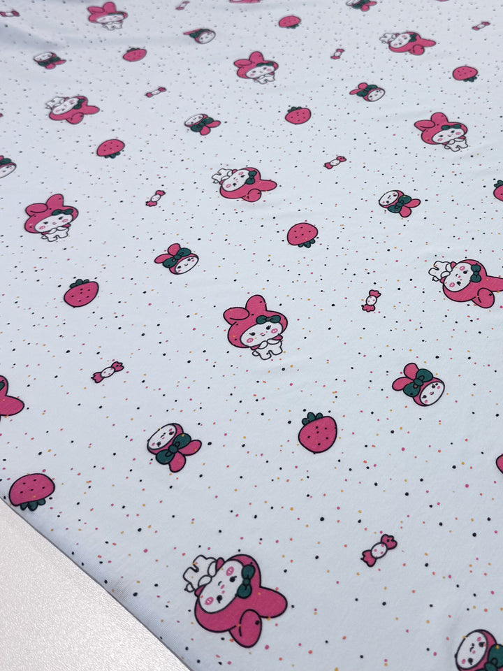 The Printed Jersey - Melody by Super Cheap Fabrics features cute cartoon characters with bow ties and strawberries on a light background with colorful dots. This medium-weight fabric offers a two-way stretch, making it versatile for various crafting projects. Width: 140cm.