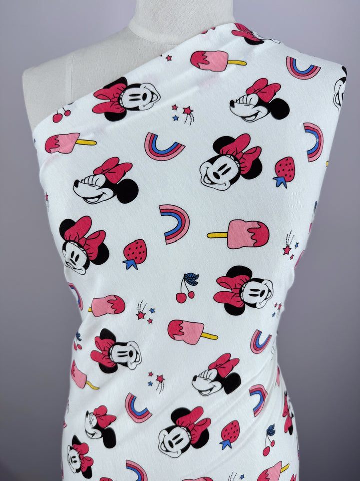 A Printed Jersey - Minni Summer by Super Cheap Fabrics drapes on a mannequin, featuring a medium-weight fabric with cartoon characters sporting bows, popsicles, strawberries, and rainbows on a crisp white background. Width: 150cm.