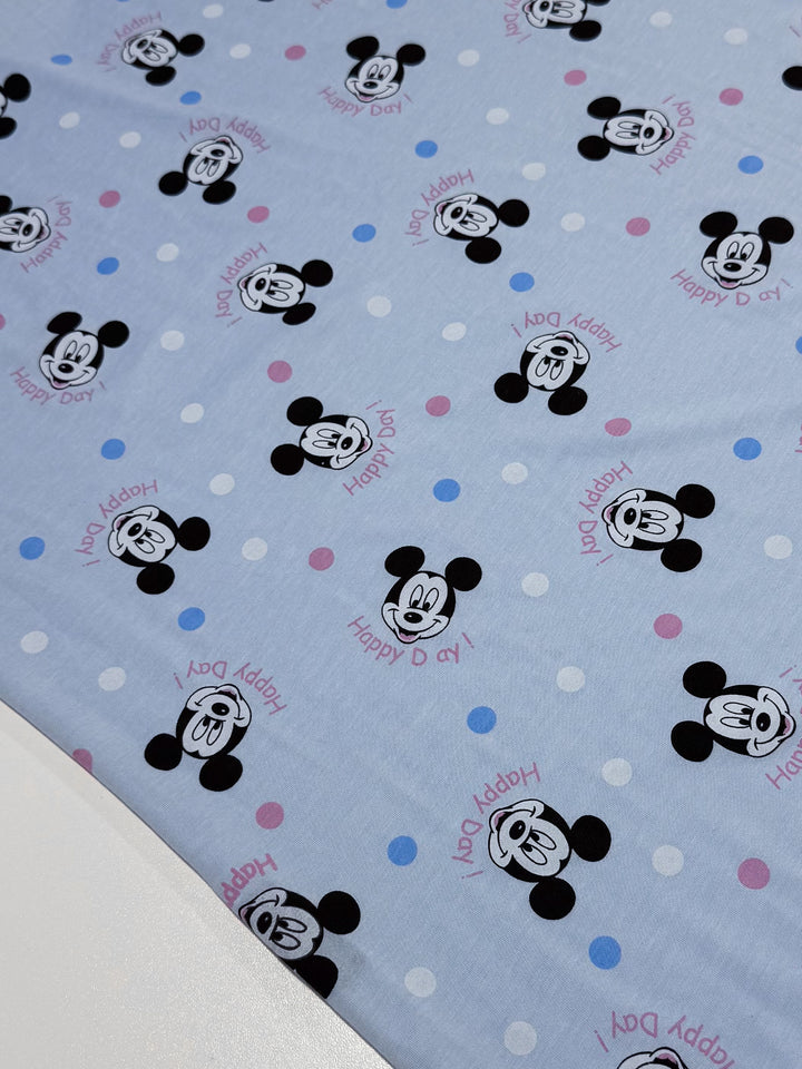 The "Printed Jersey - Cheers Ears - 150cm" by Super Cheap Fabrics features a light blue medium-weight, two-way stretch fabric adorned with cartoon mouse faces in black, red tongues, "Happy Day!" in pink and red, and scattered blue and pink polka dots.
