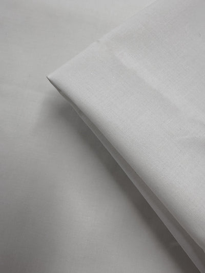 A close-up of Super Cheap Fabrics' Cotton Voile - Gardenia (150cm), neatly folded on a white surface, highlights its smooth texture and sharp edges.