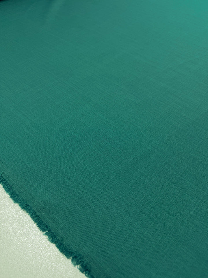 A close-up of Twill Suiting - Ivy - 150cm by Super Cheap Fabrics in teal, featuring a slightly frayed edge on the left that highlights its smooth texture, versatile use, and fine diagonal weave.