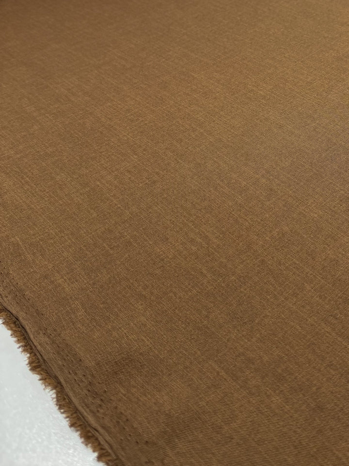 Close-up of Super Cheap Fabrics' Twill Suiting - Raw Hide, 150cm wide. The light brown polyester fabric displays a soft feel and subtle diagonal weave, with a slightly frayed edge on the bottom left corner.
