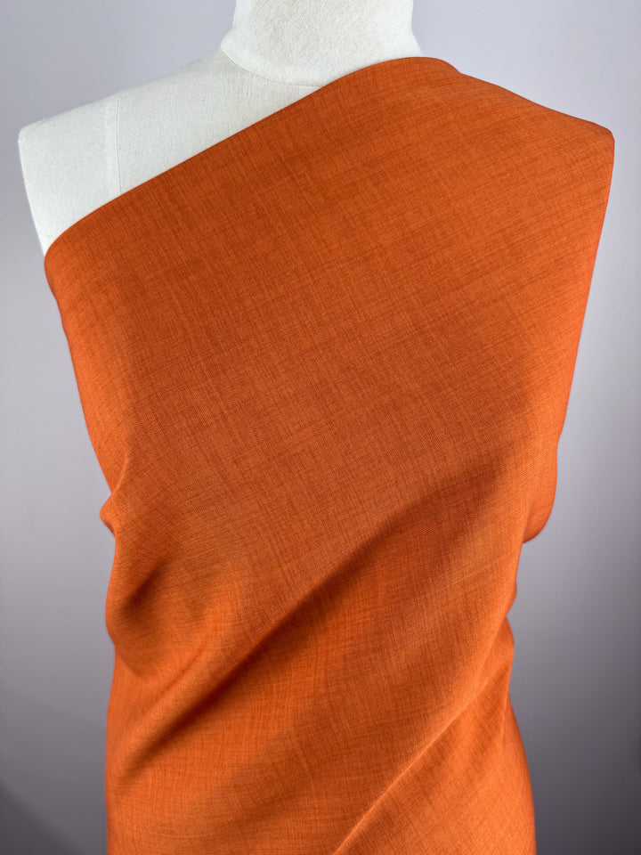 A white mannequin displays Super Cheap Fabrics’ Twill Suiting - Rust - 150cm, with the burnt orange fabric draped across one shoulder and torso, set against a neutral gray background.