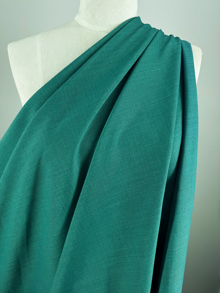 Super Cheap Fabrics’ Twill Suiting - Ivy (150cm) is shown draped elegantly over a dress form, covering one shoulder with soft folds and displaying its subtle diagonal weave for added texture and depth.