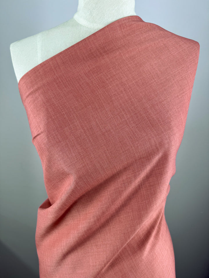 A mannequin displays Super Cheap Fabrics’ Twill Suiting - Terra Cotta (150cm), the 100% polyester fabric draped elegantly over one shoulder to showcase its smooth texture and gentle folds, set against a plain gray background.