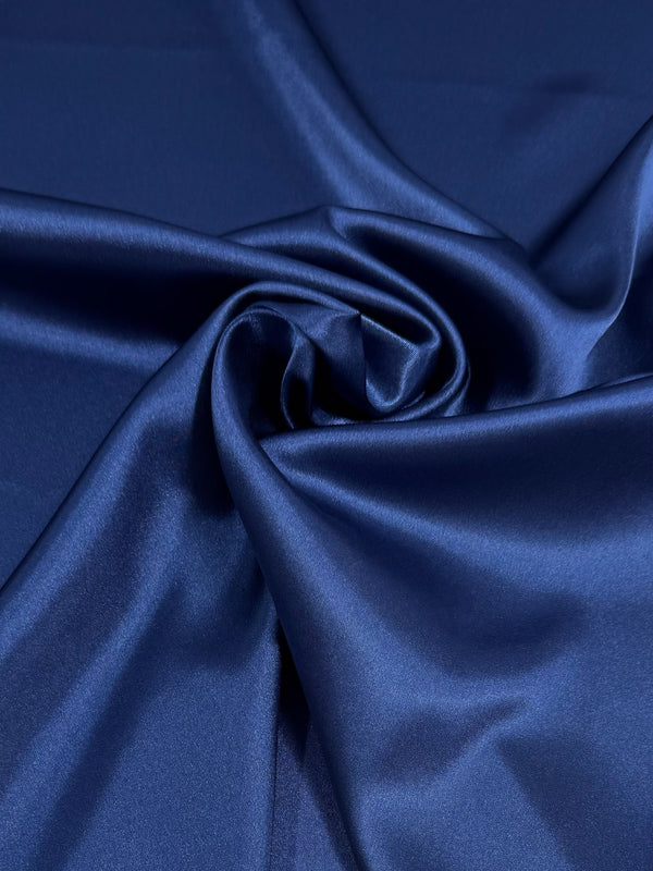 Satin Deluxe - Poseidon (150cm) by Super Cheap Fabrics features smooth, shiny deep blue satin with gentle folds and a central twist, reflecting light for a glossy, elegant texture that radiates luxury.