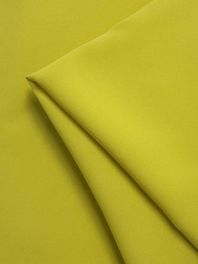 A close-up of Super Cheap Fabrics' Microfibre Suiting - Mango Mint (150cm) showcases its lightweight texture and crisp edges, neatly folded against a matching yellow background.