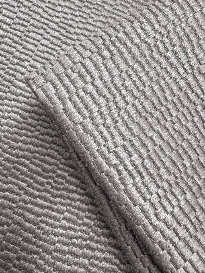 Close-up of Super Cheap Fabrics' Upholstery Jacquard - Oscar Dusk (142cm), a heavyweight silver fabric featuring a shiny, textured surface with a raised grid pattern that catches the light, emphasizing its woven structure and metallic sheen.