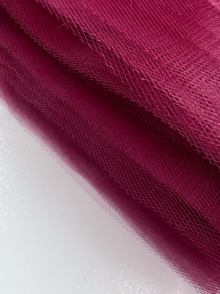 Close-up of Soft Tulle - Emboldened - 150cm by Super Cheap Fabrics, featuring maroon fine mesh layers, often used for bridal veils or costumes, draped diagonally on a white surface.