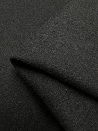 A close-up of the Wool Flannel - Black - 150cm fabric from Super Cheap Fabrics, highlighting its smooth yet slightly textured surface. The detailed shot showcases its thickness and soft texture, with the folds forming sharp angles that emphasize the heavy-weight wool material's structure and drape.