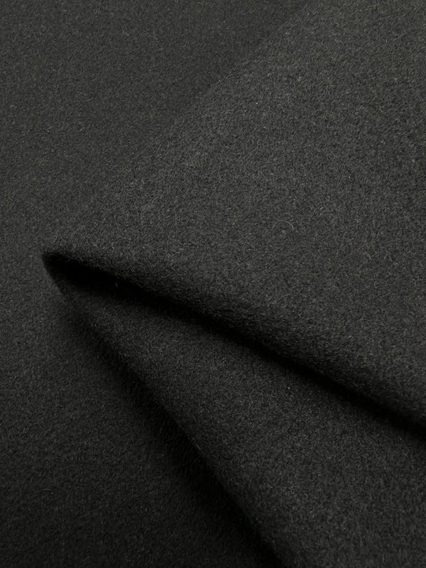 A close-up of the Wool Flannel - Black - 150cm fabric from Super Cheap Fabrics, highlighting its smooth yet slightly textured surface. The detailed shot showcases its thickness and soft texture, with the folds forming sharp angles that emphasize the heavy-weight wool material's structure and drape.