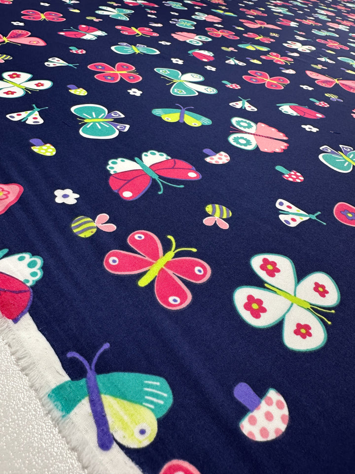 Super Cheap Fabrics presents the Printed Delustered Satin - Butterfly in a 155cm wide, dark blue fabric adorned with colorful butterflies and flowers. Featuring shades of pink, green, yellow, and white, as well as polka dots, it’s ideal for draped dresses or satins with a playful yet elegant touch.