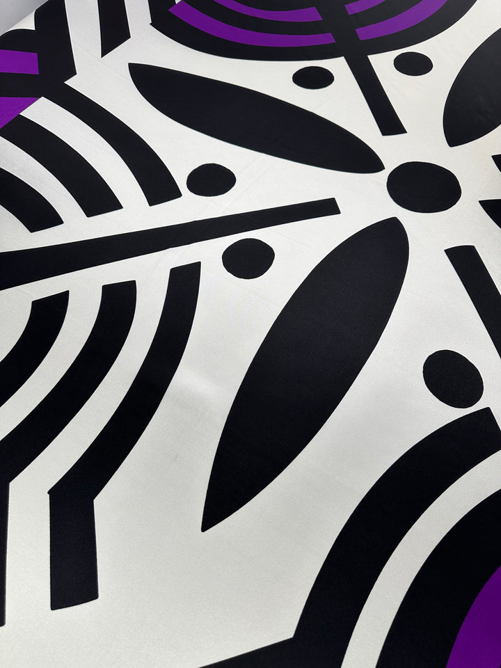 A close-up of a vibrant abstract design featuring bold black geometric shapes, including lines, circles, and ovals on a white background with accents of purple. The pattern is rendered on the luxurious Silk Twill Panel - Crop - 145cm by Super Cheap Fabrics, creating a dynamic and visually engaging composition.