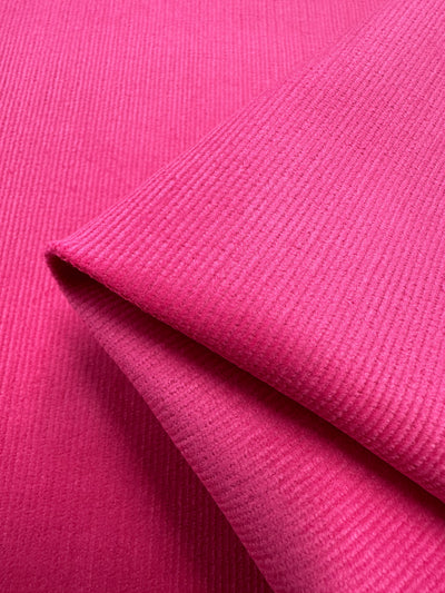 A close-up image of a piece of folded Micro Wale Corduroy in Cabaret from Super Cheap Fabrics. The fabric's distinct ribbed texture is clearly visible, showcasing the soft, velvety material and its vibrant color—perfect for elegant home decor or cozy winter clothing.