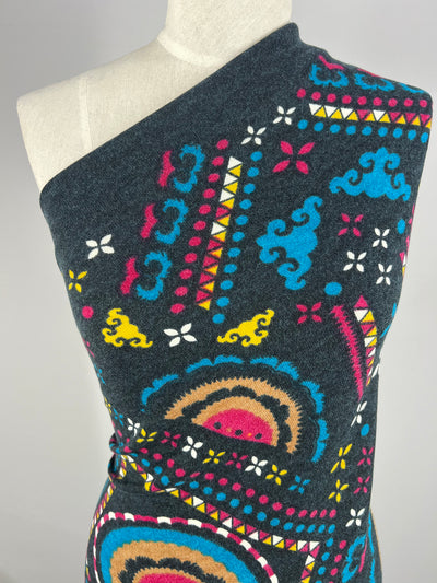A close-up of a mannequin wearing Super Cheap Fabrics' Textured Knit Panel - Shapes and Dots (80cm), showcasing colorful geometric and abstract patterns in blue, pink, yellow, white, and tan on a dark gray textured knit fabric.