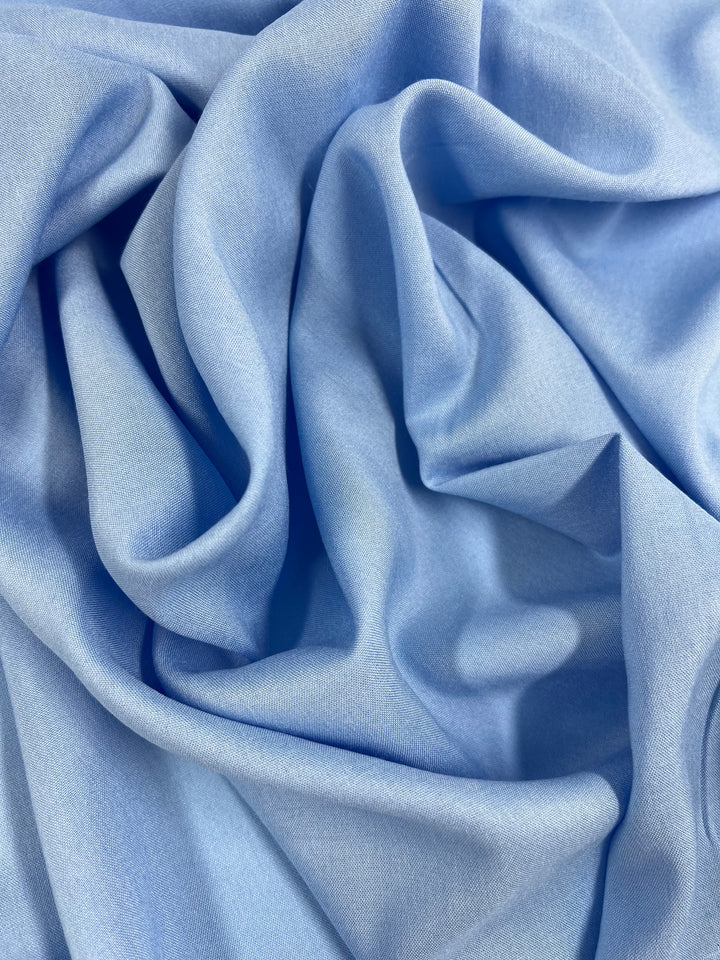 A close-up image of the Plain Rayon fabric in Blue Grotto from Super Cheap Fabrics, measuring 145cm in width, with soft, flowing folds and creases. The texture appears smooth and lightweight, showcasing the fabric draping in gentle waves.