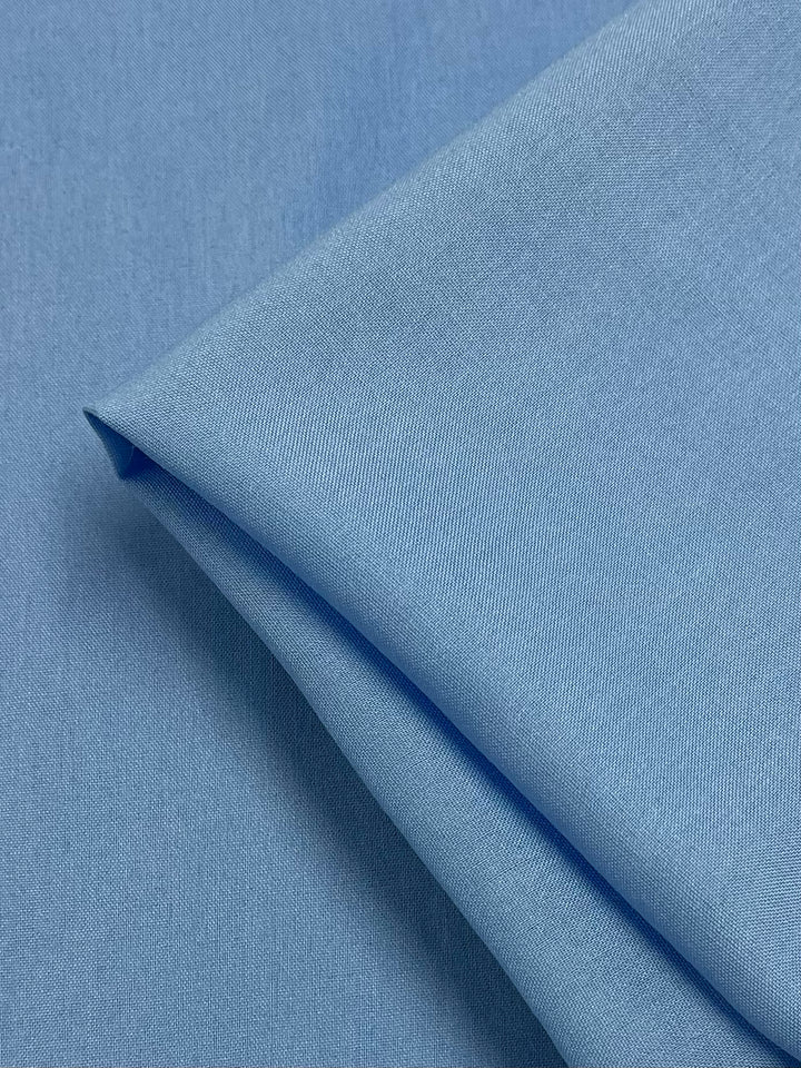 A detailed close-up of the Plain Rayon - Blue Grotto from Super Cheap Fabrics, showcasing its smooth, light blue draped and neatly folded 100% Rayon material. The texture and fibers are visible, highlighting its lightweight and refined appearance reminiscent of the serene Blue Grotto hues.