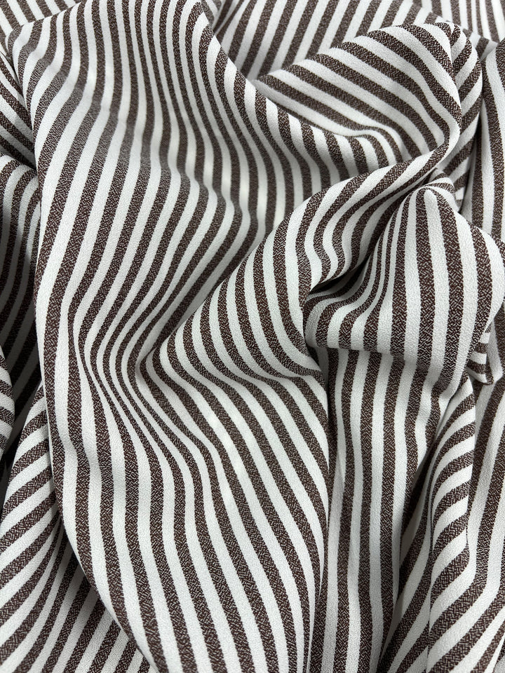 A close-up of Super Cheap Fabrics' Striped Crepe - Fondue Fudge (150cm), a lightweight polyester with wavy brown and white vertical stripes, creating an optical illusion—ideal for eye-catching eveningwear.