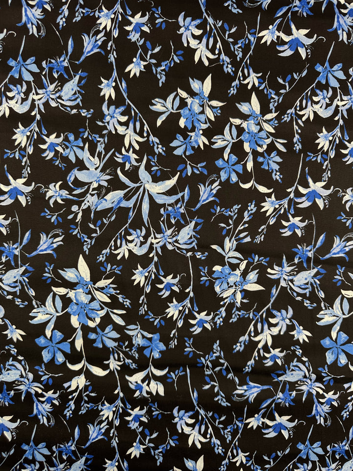Super Cheap Fabrics' Cotton Sateen - Blue Lotus (146cm) is a black and blue sateen fabric adorned with detailed blue and white floral vine patterns, plus scattered flowers in various shades of blue.