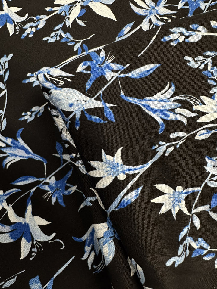 A close-up of Super Cheap Fabrics’ Cotton Sateen - Blue Lotus (146cm), a medium weight cotton spandex blend in black-blue, features blue and white lotus floral patterns with gentle creases and subtle folds.