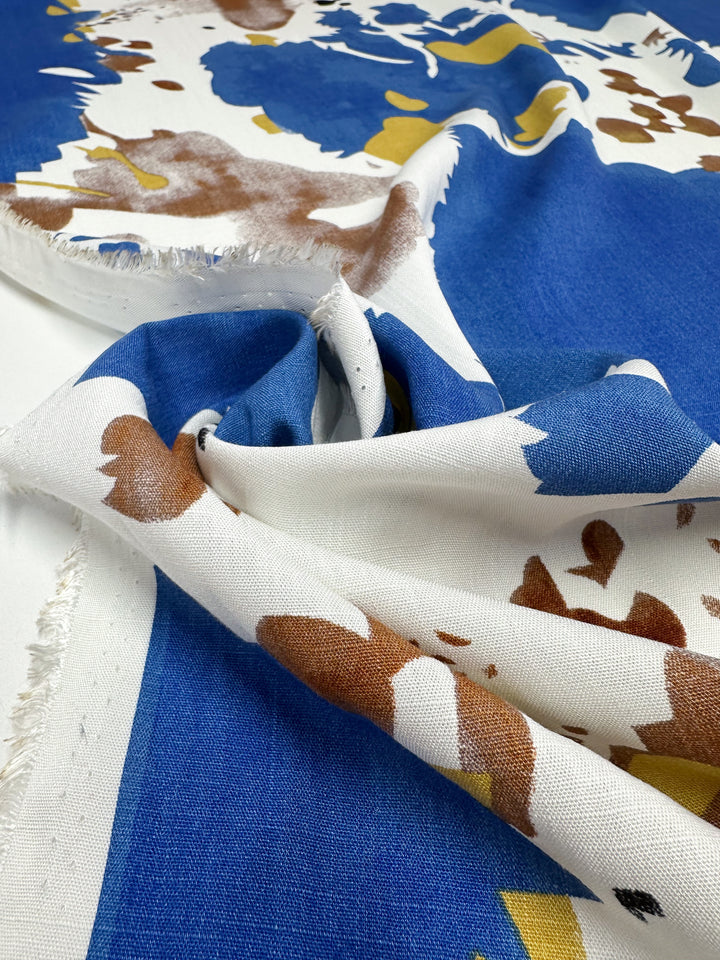 A close-up of Super Cheap Fabrics' Bamboo Rayon - Splash (150cm), featuring blue, brown, white, and yellow patterns. The lightweight fabric's texture, frayed edges, and print details make it ideal for unique sewing projects.