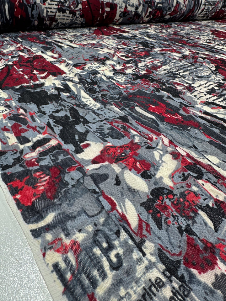 The Printed Mesh - Read - 120cm from Super Cheap Fabrics features an abstract pattern in black, red, and white. The design boasts a layered, textured appearance with scattered text and various shapes, creating a dynamic and complex visual effect. This lightweight fabric is perfect for multiple applications.