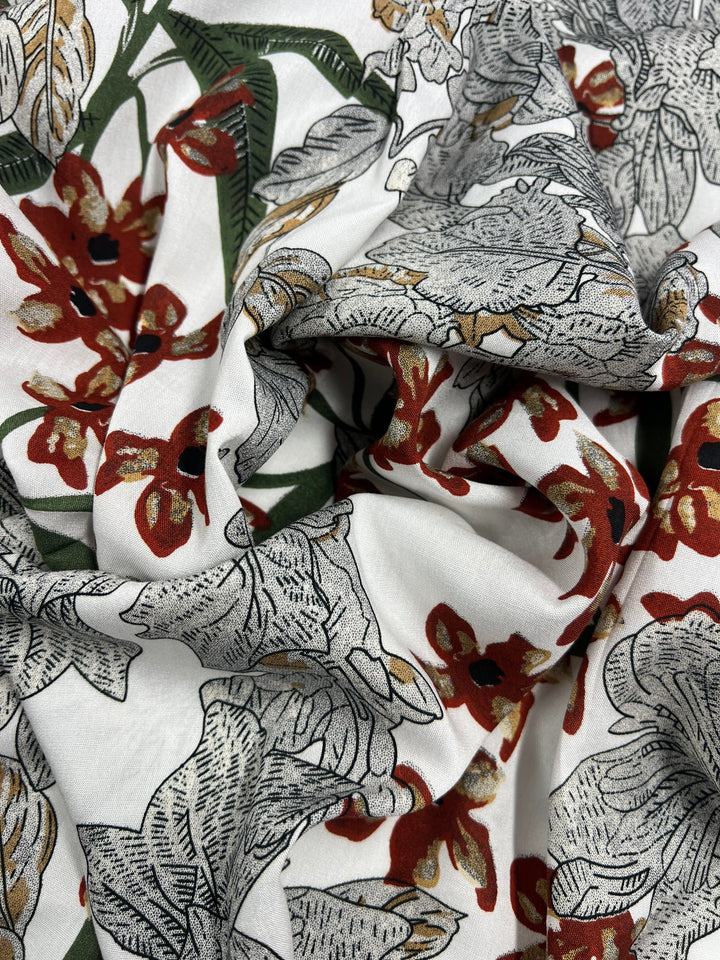 A close-up of the Super Cheap Fabrics' Printed Rayon - XL Flora - 145cm, showcasing a multi-use fabric with an intricate floral pattern. The design features large, elaborate flowers in vibrant shades of red, green, and gray set against a crisp white background. The slightly crumpled texture adds depth to the image.